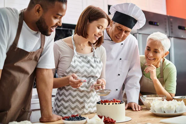 Fröhliche junge Frau in legerer Kleidung, die neben ihrer Lehrerin und diversen Freundinnen Kuchen dekoriert — Stockfoto