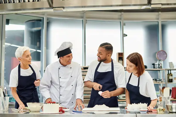 Jolly handsome african american chef breaking egg and at his joyful chief cook and colleagues — Stock Photo