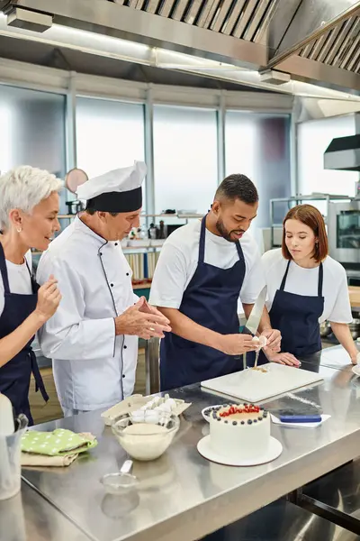 Joyeux femmes et chef cuisinier en chapeau blanc regarder leur collègue afro-américain casser oeuf — Photo de stock