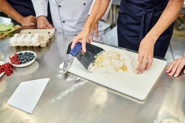 Vista ritagliata di cuoca matura che lavora con pasta accanto ai suoi colleghi, pasticceria — Foto stock