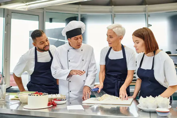 Bom olhar cozinheiro chefe maduro em chapéu branco explicando como assar para seus chefs, confeitaria — Fotografia de Stock