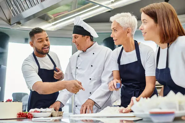 Good looking african american man in apron talking to his colleagues while they working with dough — Stock Photo