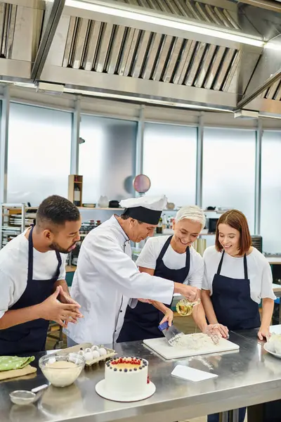 Good looking mature chef pouring oil in dough surrounded by his diverse colleagues, confectionary — Stock Photo