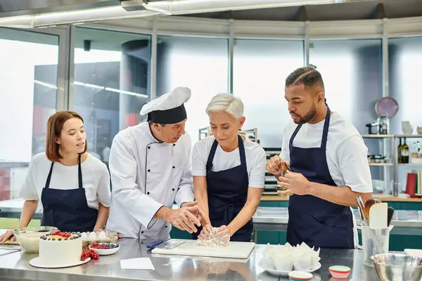 Bello maturo capo cuoco aiutare i suoi chef multiculturali con pasticcini, pasticceria — Foto stock