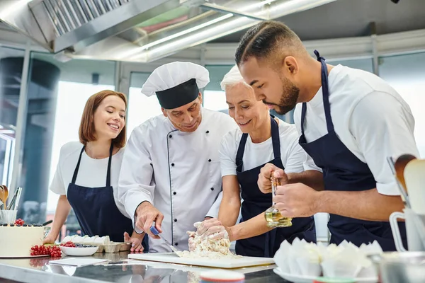 Joyous multiracial chefs in aprons working with dough together with their chief cook, confectionary — Stock Photo