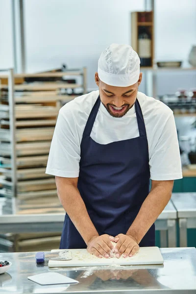 Handsome joyous african american chef in apron with toque and braces working with dough attentively — Stock Photo