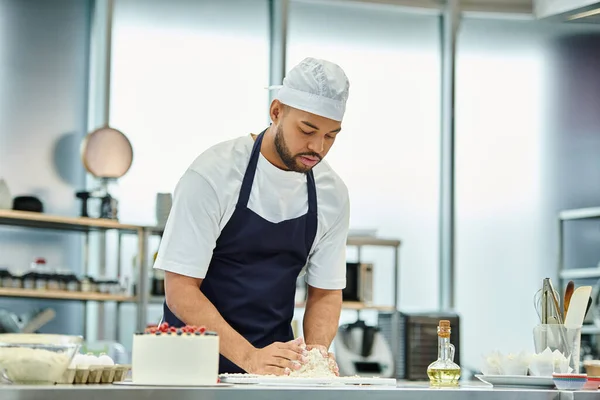 Handsome young african american chef in toque and blue apron working with dough, confectionary — Stock Photo