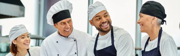 Joven chef afroamericano con toque y frenos sonriendo a sus colegas junto al jefe de cocina, pancarta - foto de stock