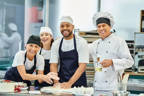 Gioiosi chef multiculturali e cuoco capo in toques sorridenti alla macchina fotografica mentre si lavora con la pasta — Foto stock
