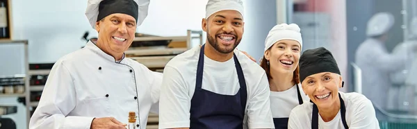Chefs alegres y diversos jefe de cocina sonriendo a la cámara mientras se trabaja con masa, confitería, pancarta - foto de stock