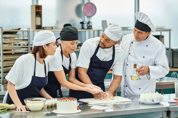 Multicultural chefs working with dough together next to chief cook holding oil, confectionery — Stock Photo