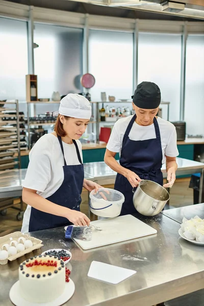 Belle chef femminili in grembiuli blu e toques che lavorano insieme con pasta, dolciumi — Foto stock