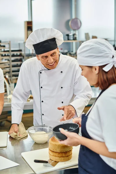 Concentrarsi sul capo cuoco maturo in cappello bianco parlando con il giovane chef sfocato in grembiule blu, pasticceria — Foto stock