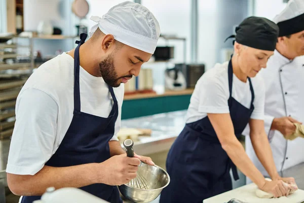 Focus on african american chef whisking ingredients next to his blurred colleague and chief cook — Stock Photo