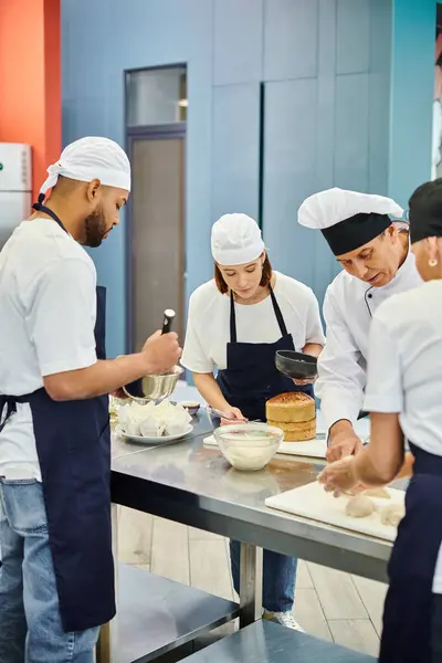 Equipo multicultural de chefs en delantales y toques que trabajan en pastelería junto con el jefe de cocina - foto de stock