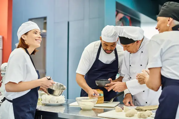 Chefs alegres sonriendo junto a su colega afroamericano y jefe de cocina trabajando en pastelería - foto de stock