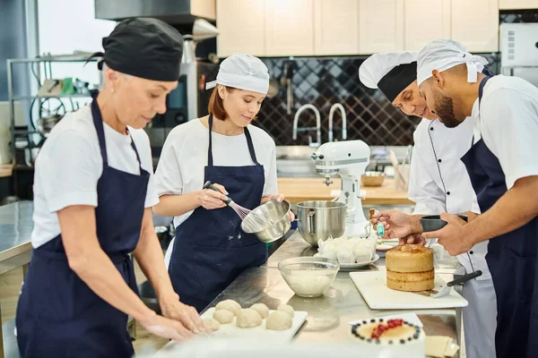 Gioiosa squadra multirazziale di chef con il loro capo cuoco che lavora sulla pasticceria insieme, pasticceria — Foto stock