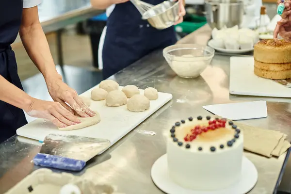 Cropped view of mature chef in apron working on dough next to her young colleague, confectionery — Stock Photo