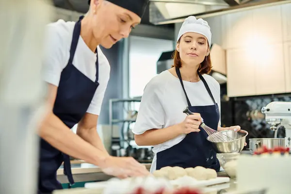 Jovem chef atraente em avental assistindo seu colega maduro trabalhando na massa, confeitaria — Fotografia de Stock