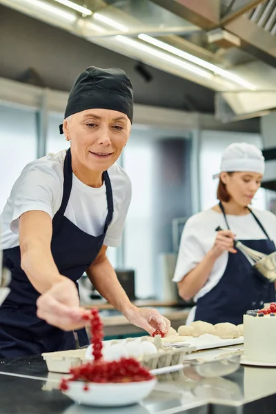 Se concentrer sur le chef joyeux mature prenant groseille rouge avec sa jeune collègue floue sur fond — Photo de stock