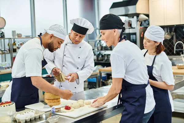 Chefs multirraciales con su jefe de cocina en sombrero blanco hornear juntos en la cocina, confitería - foto de stock
