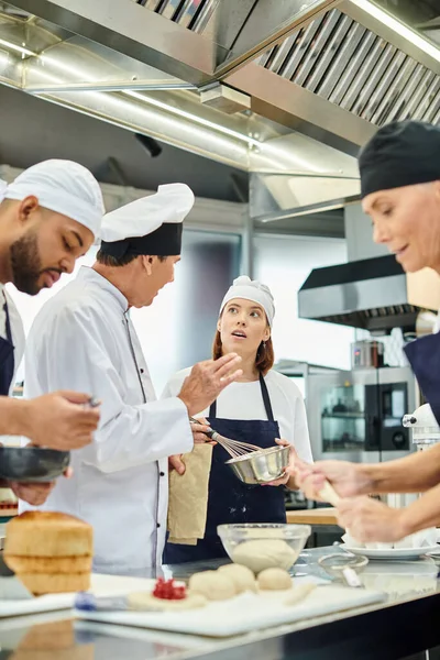 Pensativa chef femenina en toque escuchando atentamente a jefe de cocina junto a sus diversos colegas - foto de stock