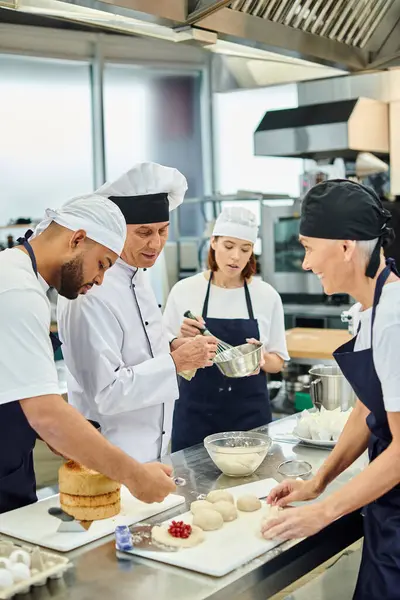 Beau chef cuisinier mature en chapeau blanc travaillant avec son équipe de chefs interracial, confiserie — Photo de stock
