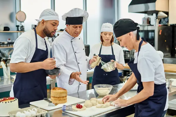 Alegre cocinero jefe maduro con sus chefs multiculturales viendo mujer madura trabajando con la masa - foto de stock