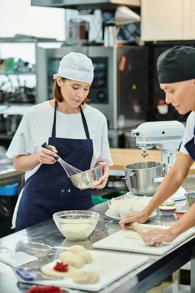 Hermosas cocineras femeninas en toques azules y delantales trabajando juntos en su masa, confitería - foto de stock
