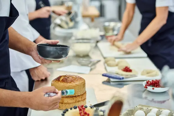 Cropped view of african american chef using silicone brush on cake next to blurred colleagues — Stock Photo