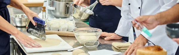 Vue recadrée de chefs travaillant dur dans des tabliers travaillant avec de la pâte sur la cuisine, confiserie, bannière — Photo de stock