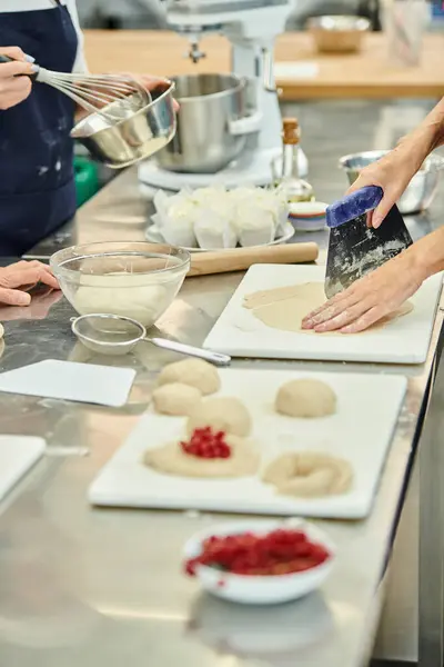Cropped view of team of chefs in blue aprons working together with dough on kitchen, confectionery — Stock Photo