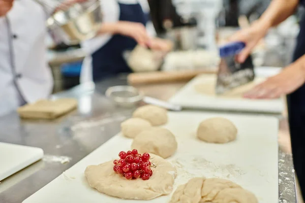 Focused view of undercooked biscuit with red currant on table next to chefs and chief cook — Stock Photo
