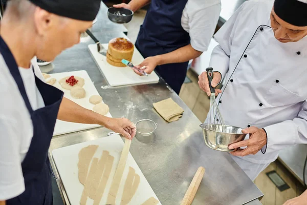Bei cuochi multirazziali in grembiuli che lavorano insieme con pasta sulla cucina, dolciumi — Foto stock