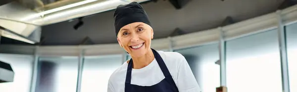 Hermosa mujer madura chef en toque azul y delantal sonriendo a la cámara, confitería, pancarta - foto de stock