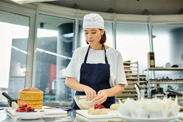 Attractive young female chef in toque and apron working hard on kitchen with dough, confectionery — Stock Photo