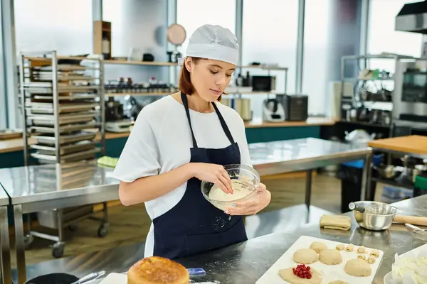 Приваблива молода жінка-шеф-кухарка в фартусі і ладі уважно працюють з тістом, кондитерські вироби — стокове фото