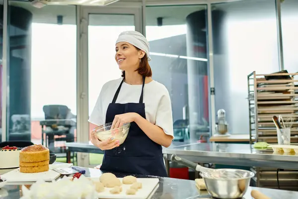 Весела молода жінка-шеф-кухарка в фартусі, що працює з тістом, посміхається і дивиться, кондитерські вироби — стокове фото