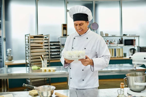 Joyeux beau chef cuisinier mature en chapeau blanc tenant des cupcakes et souriant joyeusement, confiserie — Photo de stock
