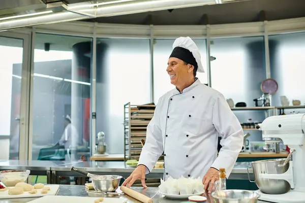 Gioioso bel capo cuoco maturo in cappello bianco sorridente felicemente e distogliendo lo sguardo, pasticceria — Foto stock