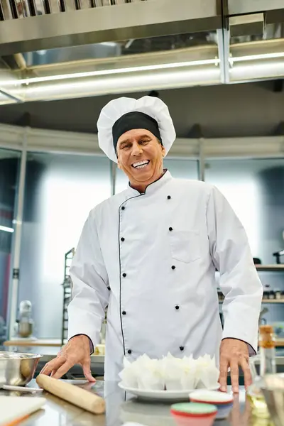 Alegre cocinero jefe maduro en sombrero blanco sonriendo a la cámara mientras hornea en la cocina, confitería - foto de stock