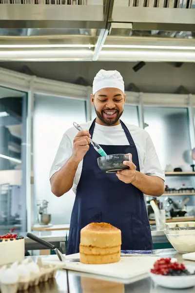 Alegre joven guapo afroamericano chef en toque usando cepillo de silicona y sonriendo felizmente - foto de stock