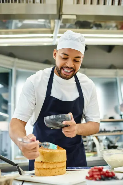 Jovem chef americano africano alegre em avental e toque usando escova de silicone em bolo, confeitaria — Fotografia de Stock