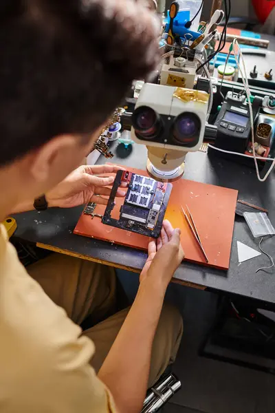 Розмитий ремонтник, дивлячись на мікросхему сучасного електронного пристрою на робочому місці в ремонтному магазині — стокове фото