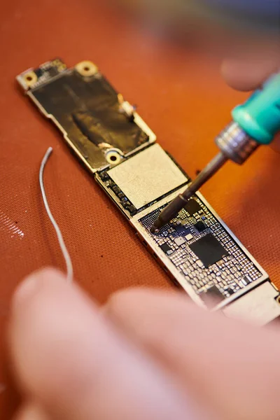 Ausgeschnittene Ansicht eines Technikers beim Löten eines Chipsatzes eines modernen elektronischen Geräts in einer privaten Werkstatt — Stockfoto