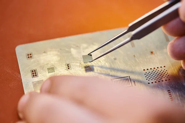 Vista ritagliata di riparatore esperto con pinzette e chip vicino al circuito elettronico in officina — Foto stock
