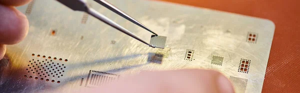 Vista parcial de reparador experto con pinzas y chip cerca del circuito electrónico en el taller, pancarta - foto de stock