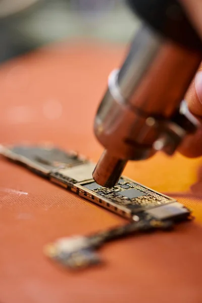 Ausgeschnittene Ansicht eines qualifizierten Technikers, der Chip mit Mikroskop in der Werkstatt untersucht, Reparaturgeschäft — Stockfoto