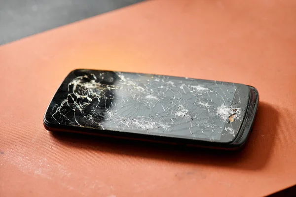 Современный мобильный телефон со сломанным сенсорным экраном на столе в ремонтной мастерской, техническое обслуживание оборудования — стоковое фото