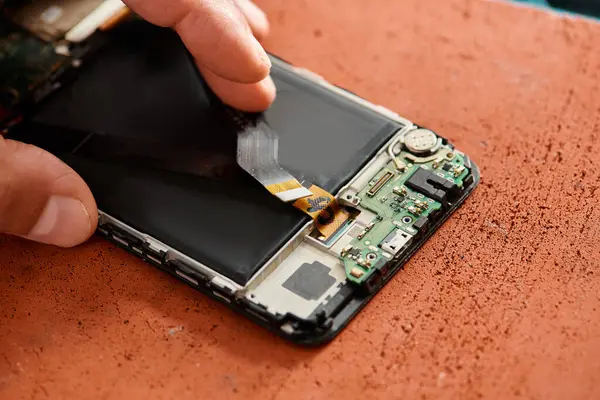 Vue partielle du technicien expérimenté retirant la batterie du téléphone portable dans l'atelier, entreprise de réparation — Photo de stock